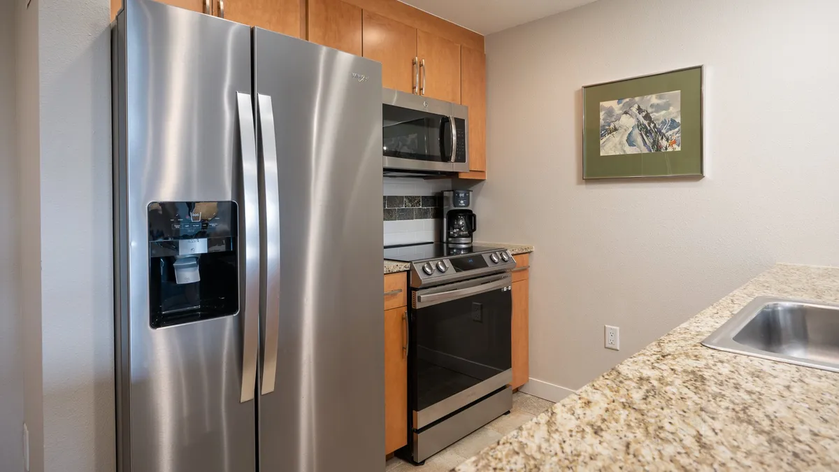 A bright, modern kitchen featuring a stainless steel refrigerator, modern stove, granite countertop, and framed artwork. The space is designed with both functionality and style in mind, creating an inviting atmosphere for meal preparation and gathering.