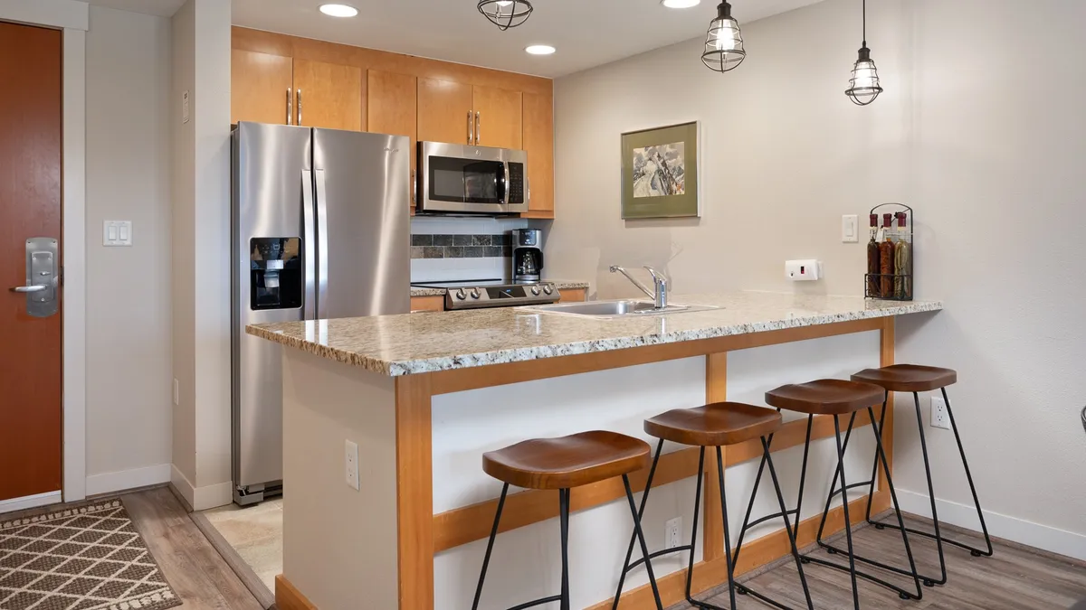 A modern chef's kitchen with a large island, bar stools for casual seating, stainless steel appliances, and framed artwork. The design is bright and inviting, ideal for cooking, entertaining, or sharing stories over snacks.