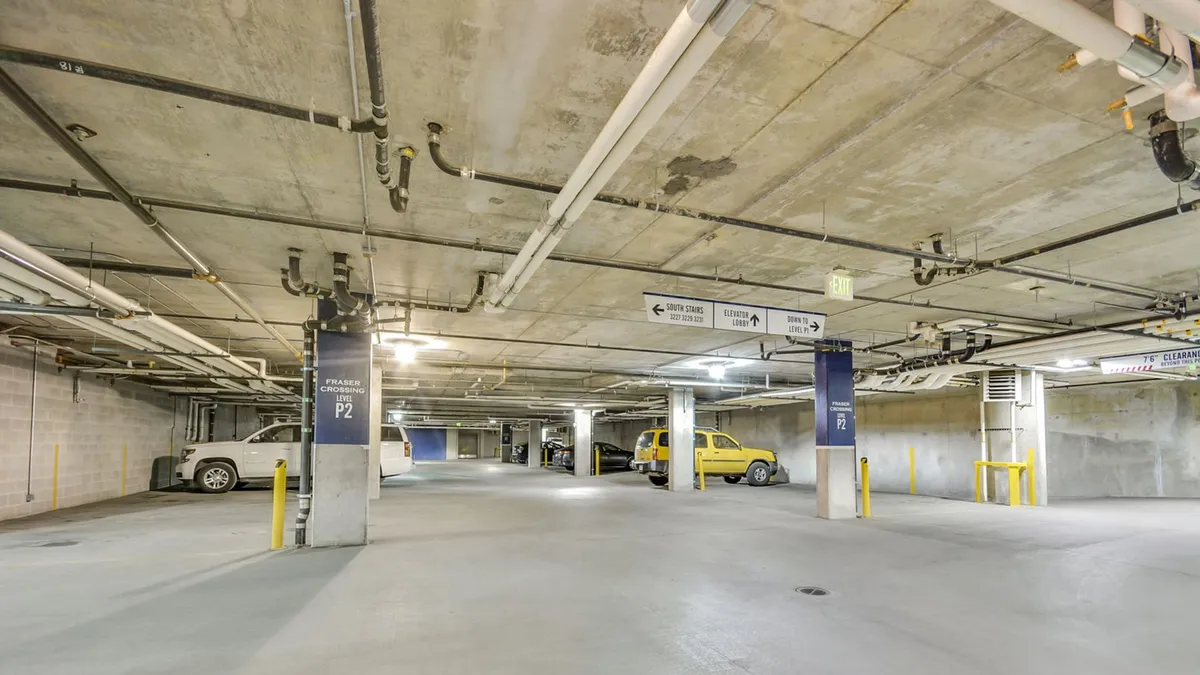A heated underground parking garage with concrete pillars, clear signage, and yellow parking barriers. Vehicles are parked neatly, highlighting the security and convenience of direct garage access during winter or summer stays.