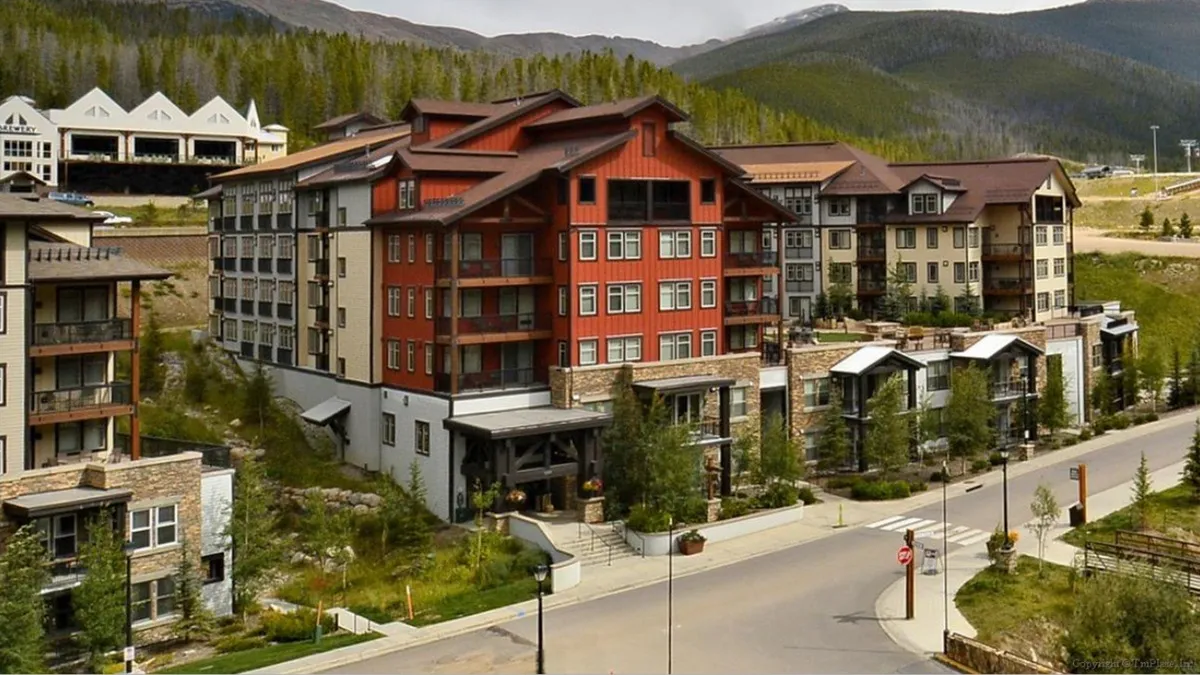This exterior shot highlights a red building with a stone façade, surrounded by towering trees. The mood is welcoming and serene, hinting at opportunities for sunset views from balconies and stargazing in tranquil outdoor spaces.