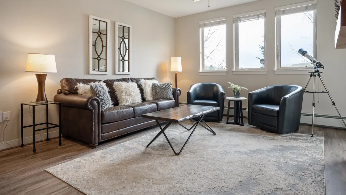 A comfortable, alpine-inspired living area featuring a plush sofa, coffee table, armchairs, and a telescope by the window. The space is designed for relaxation, reading, or stargazing, with a warm, welcoming ambiance.