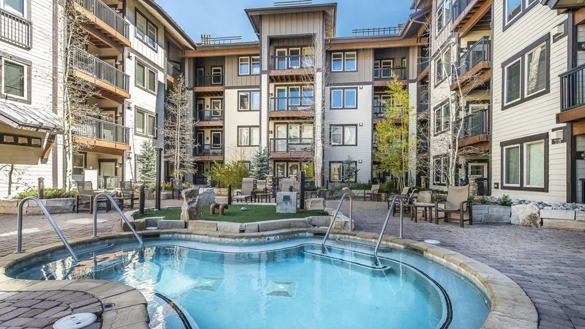 The exterior view showcases a sunlit swimming pool surrounded by lounge chairs, landscaped grounds, and apartment buildings. Groups are swimming, sunbathing, and socializing, with a relaxed summer resort vibe.